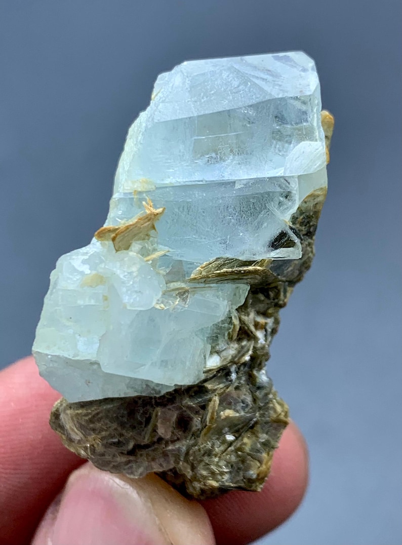 Peut inclure: Sp&eacute;cimen brut de cristal d'aigue-marine. Le cristal bleu p&acirc;le est partiellement transparent et repose sur une matrice de min&eacute;raux bruns et beiges. Le cristal a un aspect stratifi&eacute; avec des facettes visibles et une texture naturelle non polie.