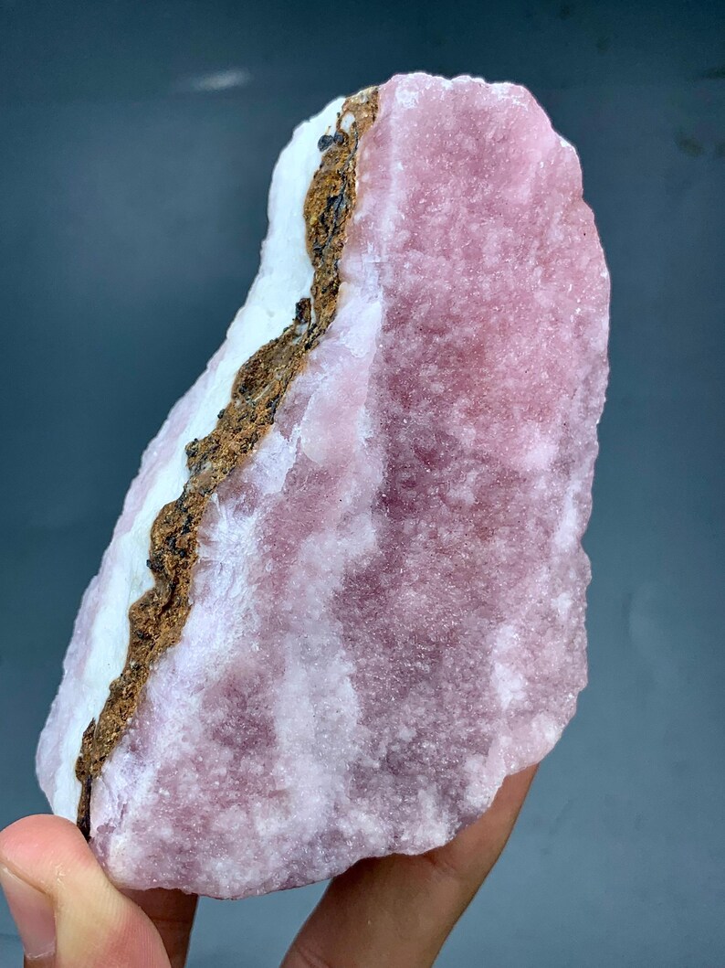 May include: A large, rough-hewn mineral specimen with a prominent pink hue. The stone features a white section and a brown, textured band. The overall appearance is natural and unpolished, showcasing the raw beauty of the mineral.