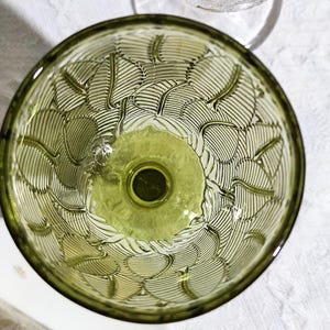 May include: An overhead view of a green glass bowl with a leaf pattern etched into the interior. The bowl has a circular base and a wide, shallow rim. The leaf pattern is detailed and covers the entire interior surface.