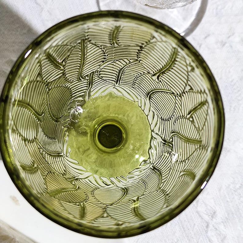 May include: An overhead view of a green glass bowl with a leaf pattern etched into the interior. The bowl has a circular base and a wide, shallow rim. The leaf pattern is detailed and covers the entire interior surface.