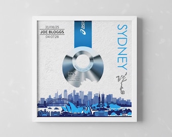 May include: Framed print featuring a blue and silver marathon medal with the text "Sydney" and a skyline silhouette. Includes the date 31/08/25, name "JOE BLOGGS", and time 04:07:28. The print is in a white frame.