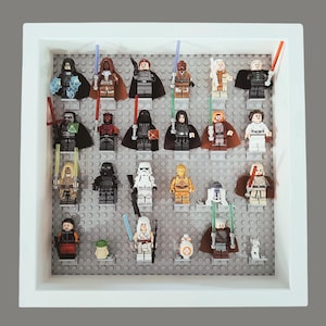 May include: A framed display of various Lego Star Wars minifigures. The figures are arranged on gray Lego baseplates within a white frame. The collection includes characters with lightsabers and other accessories, showcasing a variety of colors and designs.