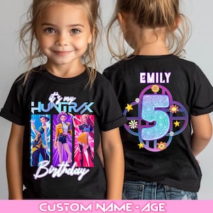 Może przedstawiać: Czarny t-shirt z kolorową grafiką przedstawiającą trzy animowane postacie i napisem "It's my Huntrix Birthday". Tył koszulki przedstawia imię "Emily" nad dużą cyfrą "5" z kwiatowymi i gwiazdkowymi akcentami. Koszulka z motywem urodzinowym.