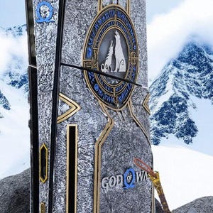 May include: A custom console skin featuring a textured grey stone finish with gold trim and blue accents. The design includes a circular emblem with two wolves, runic inscriptions, and the text "GOD OF WAR" with a blue omega symbol.