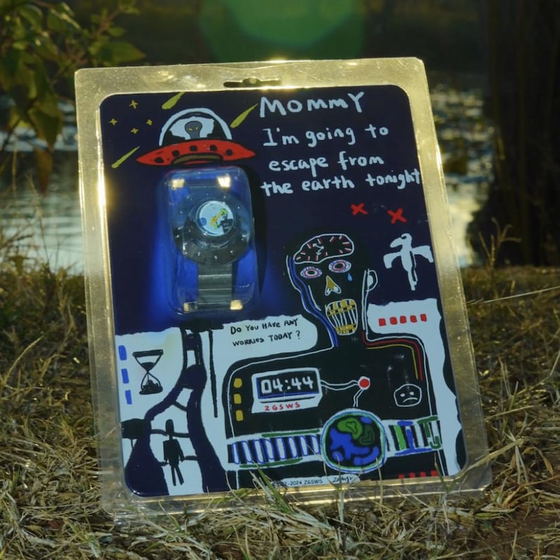 May include: A wristwatch in clear plastic blister packaging featuring a dark blue card with a hand-drawn style illustration of a UFO, a figure, and text that reads: Mommy I'm going to escape from the earth tonight and Do you have any worries today?