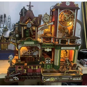 May include: A multi-level wooden model kit featuring a clock tower, a train, and a conveyor belt. The structure includes illuminated details, gears, and signs labeled "COUNTER JOY TIME OFFICE," "PACKAGE," and "CONVEYOR." A small figure on a bicycle is positioned near the conveyor section, with intricate architectural elements and warm lighting throughout the display.