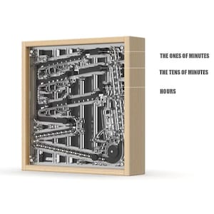 May include: A square wall clock with a light wood frame containing a complex mechanical system of silver metal tracks and black chains. Text labels indicate the sections for THE ONES OF MINUTES, THE TENS OF MINUTES, and HOURS within the mechanism.