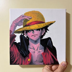 Può includere: Un dipinto di un personaggio della serie anime One Piece. Il personaggio indossa un cappello di paglia, una giacca rossa e ha i capelli neri. L'opera d'arte è su una tela bianca.