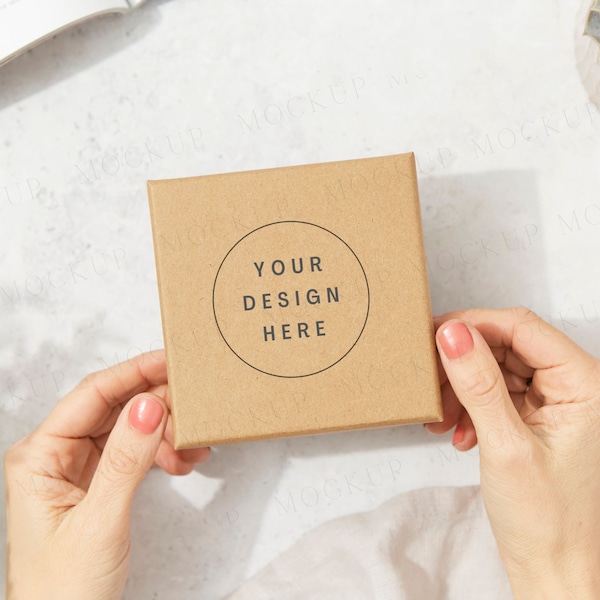 Kraft brown jewelry box packaging mockup with hands and plants. Dappled sunlight, sunny day. Cardboard postage box jewellery mockup.