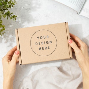 May include: A person holds a brown cardboard box with the text "YOUR DESIGN HERE" printed in a circle on the front.