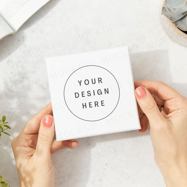 White jewelry box packaging mockup with hands and plants. Dappled sunlight, sunny day. White cardboard postage box jewellery mockup.