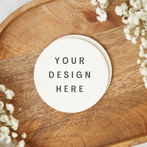 May include: A white round coaster with the text "YOUR DESIGN HERE" on a wooden tray with white flowers.
