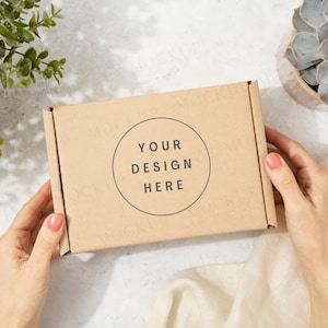 Mockup di confezione regalo con mani e pianta. Mockup di scatola di spedizione marrone Kraft con modello a mano. Sole screziato, giornata di sole.
