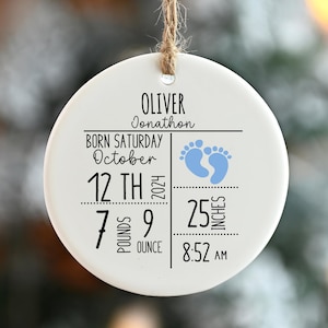 May include: A white ceramic ornament with the name "Oliver Jonathan" and birth details. The ornament includes the date, time, weight (7 pounds 9 ounces), and length (25 inches) of a newborn baby, along with blue footprints.