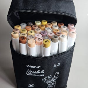 Könnte beinhalten: Eine schwarze Reißverschlusstasche mit Ohuhu Honolulu Alkoholmarkern. Die Marker haben weiße Schäfte und verschiedenfarbige Kappen. Auf der Tasche befinden sich der Markenname und eine Froschillustration. Das Set enthält 36 Marker.