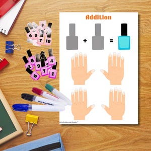 Può includere: Un foglio di attività didattiche con la parola "Addition" in alto, che illustra problemi di addizione con flaconi di smalto per unghie e mani. Carte numeriche di smalto per unghie e pennarelli su una superficie di legno.