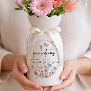 Könnte beinhalten: Eine weiße Keramikvase mit cremefarbenem Band, gefüllt mit rosa Gerbera, Tulpen und anderen Blumen. Die Vase trägt den Text "If grandmas were flowers, I'd pick you."