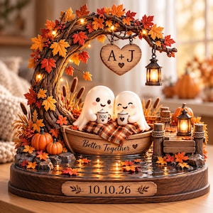 May include: A decorative autumn-themed display featuring two white ghost figurines in a wooden boat, holding mugs labeled 'BOO' and a heart. The boat is inscribed with 'Better Together' and sits on a base with '10.10.26' and maple leaves.