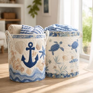 May include: Two cylindrical fabric storage baskets featuring quilted nautical designs. The left basket displays a large blue anchor, seashells, and blue waves. The right basket features blue sea turtles, starfish, and seaweed patterns.