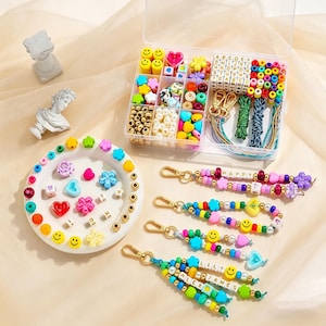 May include: A craft kit with colourful beads, smiley faces, and letter beads. The kit includes a clear plastic organiser, gold-coloured clasps, and finished beaded keychains with names like "HAPPY" and "LILY JAMES".