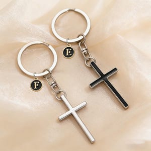 Peut inclure: Deux porte-clés avec des pendentifs en forme de croix. Une croix est argentée, l'autre est noire. Chaque porte-clés a un charme circulaire avec une lettre, l'un avec "E" et l'autre avec "F". Les anneaux sont argentés.