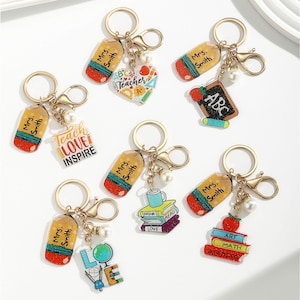 May include: A selection of teacher-themed keyrings. Each keyring includes a gold-coloured ring, a pencil-shaped tag with "Mrs. Smith" printed on it, and a charm with school-related designs, such as an apple, books, and a globe.