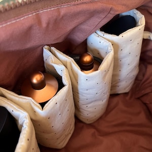 Pu&ograve; includere: Vista aperta di una borsa da viaggio marrone con cerniera. All'interno, ci sono diverse tasche in tessuto color crema con piccoli pois neri. Le tasche contengono oggetti color rame. L'interno della borsa &egrave; marrone rossiccio.