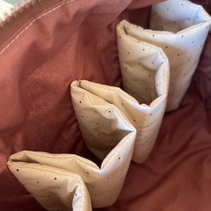 Pu&ograve; includere: Vista interna di una borsa con cerniera color rosa polvere con pi&ugrave; tasche color crema a pois. Le tasche sono piegate e cucite nella fodera della borsa. L'interno della borsa &egrave; di un colore rosa polvere uniforme.