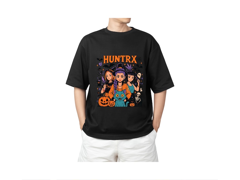 May include: Black t-shirt with a Halloween graphic, featuring the word "HUNTRX" in orange. The design includes three cartoon figures, pumpkins, a black cat, and other spooky elements. The shirt is worn by a person.