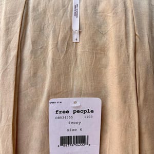 May include: Close-up of a cream-colored garment with a tag from Free People. The tag indicates the size is 6 and the color is ivory. The suggested retail price is $128.00.