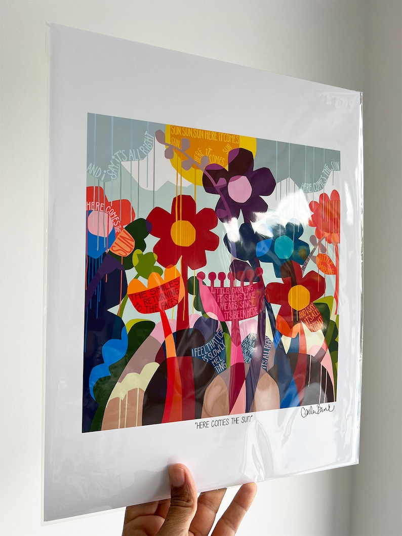Puede incluir: Una impresi&oacute;n de arte abstracto colorida con un tema floral. La impresi&oacute;n presenta una variedad de flores en tonos de rojo, naranja, amarillo, morado y azul. El fondo es azul claro con acentos blancos y amarillos. El texto "Here Comes The Sun" est&aacute; impreso en la parte inferior de la impresi&oacute;n.
