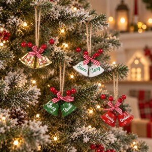 Peut inclure: Quatre paires de clochettes suspendues sur un sapin de Noël. Chaque paire comporte deux cloches attachées avec un ruban à carreaux rouge et blanc, des aiguilles de pin vertes et des baies rouges. Les cloches sont dorées, blanches, vertes et rouges.
