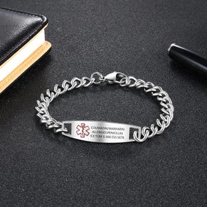 May include: A silver-colored medical alert bracelet with a chain link design. The rectangular plate displays a red medical symbol and text: COUMADIN/WARFARIN, ALLERGIES: PENICILLIN, ICE: TOM G 666.555.5678.