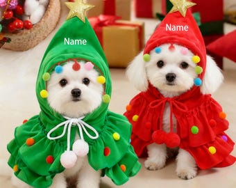 May include: Two small white dogs wearing Christmas tree costumes. One dog is in a green outfit with a gold star on its head, the other is in a red outfit. Both outfits have colorful pom-poms and the word "Name" is printed on the hats.