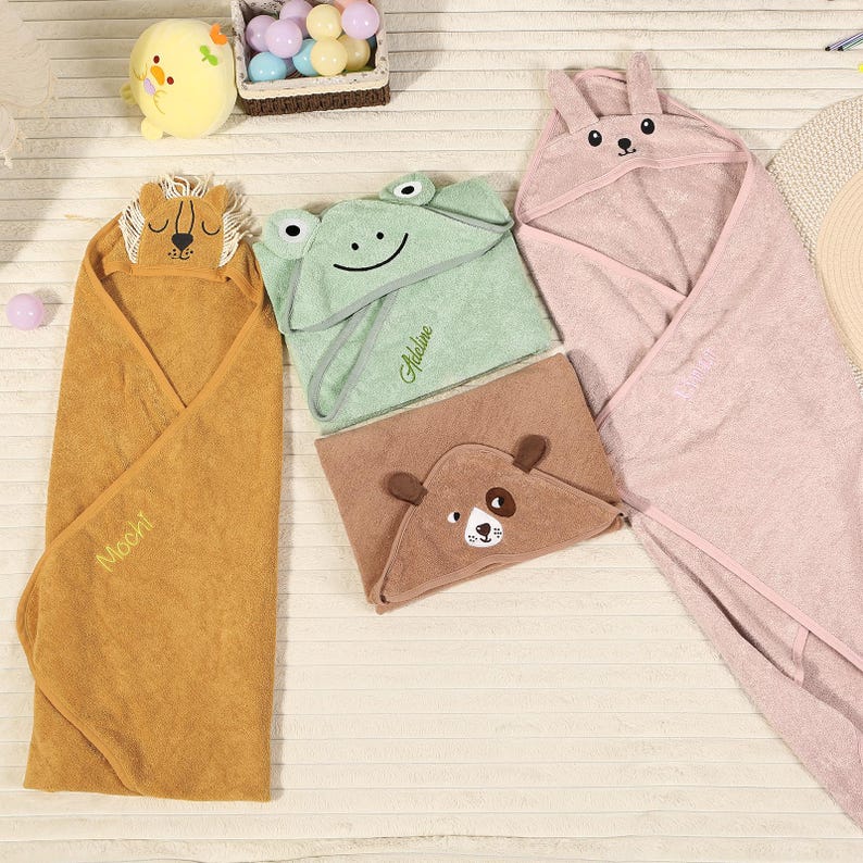 Pode incluir: Uma cole&ccedil;&atilde;o de toalhas com capuz para beb&ecirc;s em v&aacute;rias cores e designs de animais. As toalhas incluem um le&atilde;o, um sapo, um urso e um coelho. A toalha de le&atilde;o &eacute; marrom, o sapo &eacute; verde, o urso &eacute; marrom e o coelho &eacute; rosa. Cada toalha tem um capuz com um rosto de animal.