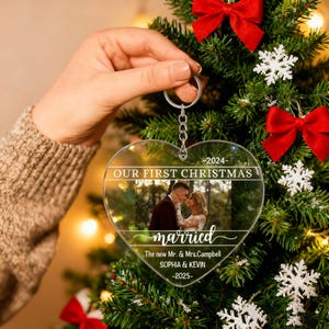 Könnte beinhalten: Transparenter herzförmiger Weihnachtsschmuck mit einem Foto eines Paares. Der Schmuck trägt den Text "OUR FIRST CHRISTMAS" und "married". Die Namen "SOPHIA & KEVIN" und die Jahre 2024 und 2025 sind ebenfalls sichtbar.