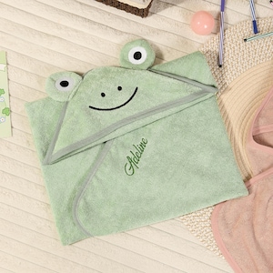 Pode incluir: Uma toalha de banho com capuz verde claro para beb&eacute; com um design de rosto de r&atilde;. A toalha apresenta um rosto sorridente, dois olhos redondos e o nome "Adeline" bordado em verde. A toalha &eacute; feita de material macio.