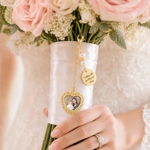 May include: A gold-toned heart-shaped photo charm attached to a bouquet handle wrapped in white satin ribbon. The charm features a small photograph and a round gold disc engraved with the text Walking with you today and always, accented by two white pearls.