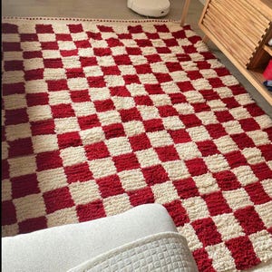 May include: A red and cream checkered rug. The rug has a thick, textured pile and a bold pattern of alternating red and cream squares. The rug is rectangular and appears to be made of a soft material.