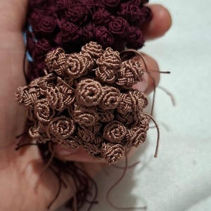 Könnte beinhalten: Nahaufnahme von zwei Bündeln handgefertigter Miniaturrosen. Ein Bündel ist tief burgunderfarben, das andere hellbraun. Die Rosen bestehen aus eng gewickeltem Faden, wobei sich lose Fäden von der Basis erstrecken.