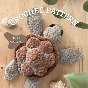 Könnte beinhalten: Ein gehäkeltes Schildkrötenmuster mit dem Text "CROCHET PATTERN" und "PEU DE COUTURE". Die Schildkröte ist aus grauem und braunem Garn gefertigt, mit einem strukturierten Panzer und Flossen. Der Hintergrund ist eine helle Holzoberfläche.