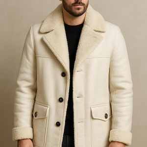 Könnte beinhalten: Cremefarbener Mantel mit Schafsfellkragen und -bündchen. Der Mantel hat eine Knopfleiste, zwei Vordertaschen und eine taillierte Passform. Das DRESSORT-Logo befindet sich in der oberen linken Ecke.