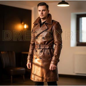 May include: A brown leather trench coat with a double-breasted design, a belt, and a wide collar. The coat has button details and is worn by a person. The word "DRESSORT" is visible in the image.