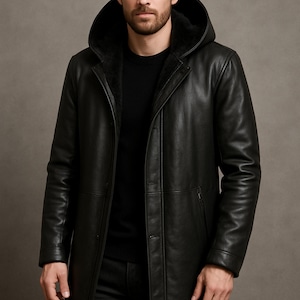 May include: Black leather hooded coat with a button-up front. The coat has a long length and a fur-lined hood. The image shows a man wearing the coat. The coat is from the brand Dressort.