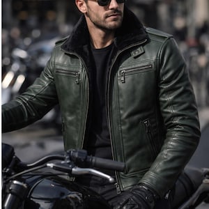 Può includere: Giacca di pelle verde scuro con colletto in pelliccia nera, indossata con guanti e occhiali da sole neri. La giacca ha più tasche con cerniera e viene indossata mentre si è seduti su una moto nera. Il logo del marchio "DRESSORT" è visibile.