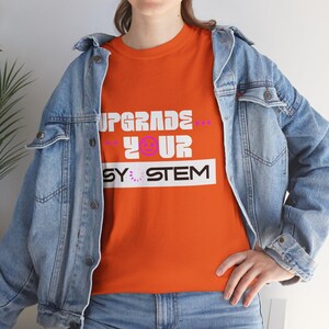 May include: Orange t-shirt with the text "UPGRADE YOUR SYSTEM" in white and purple. The shirt is worn with a blue denim jacket.