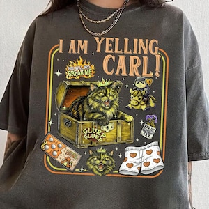 May include: Dark grey t-shirt with the text "I AM YELLING CARL!" and a graphic of a cat in a treasure chest. Additional graphics include a knight on a horse, underwear with hearts, and a box of cookies.