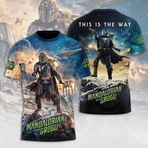 May include: A Star Wars t-shirt featuring The Mandalorian and Grogu. The front of the shirt displays a detailed image of The Mandalorian on a rocky surface, with a space scene backdrop. The back of the shirt has the text "THIS IS THE WAY".