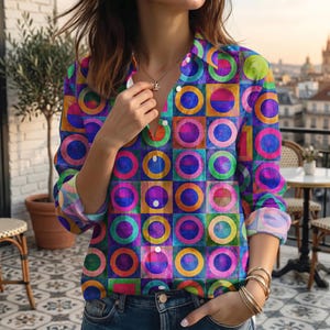 May include: A long-sleeved button-down shirt featuring a vibrant grid pattern of multicoloured squares and circles in shades of blue, purple, green, yellow, and orange. The shirt has a classic collar, white buttons, and is worn with blue denim jeans.