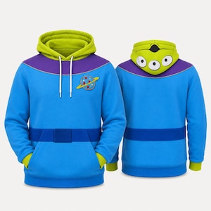 Puede incluir: Una sudadera con capucha azul que presenta una capucha verde lima con un gr&aacute;fico de cara de alien&iacute;gena de tres ojos, un panel morado en el pecho, un parche de planeta en el lado izquierdo y un gr&aacute;fico de cintur&oacute;n azul oscuro en la cintura.